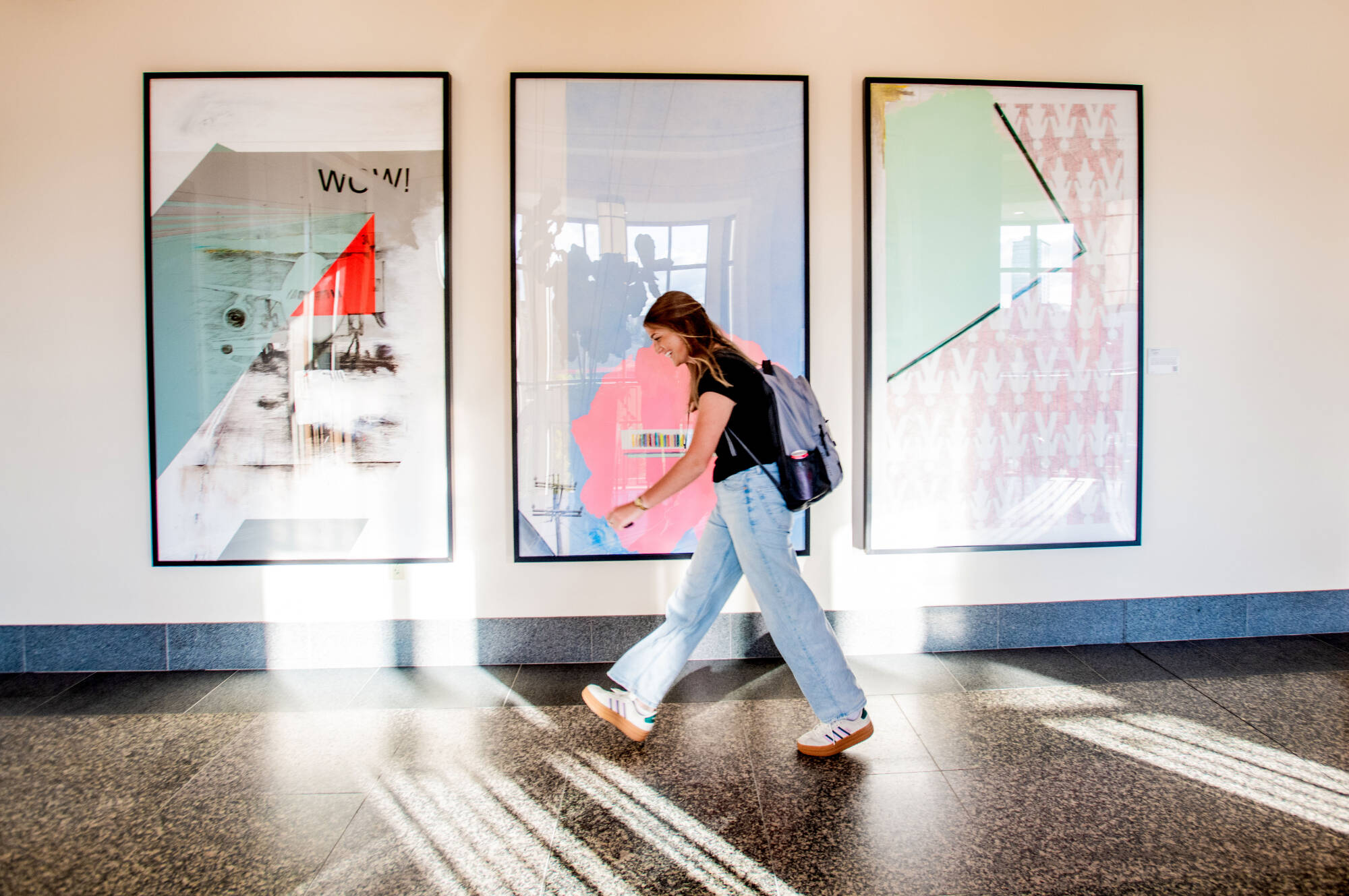 student walking through hallway, well lit with art on the walls